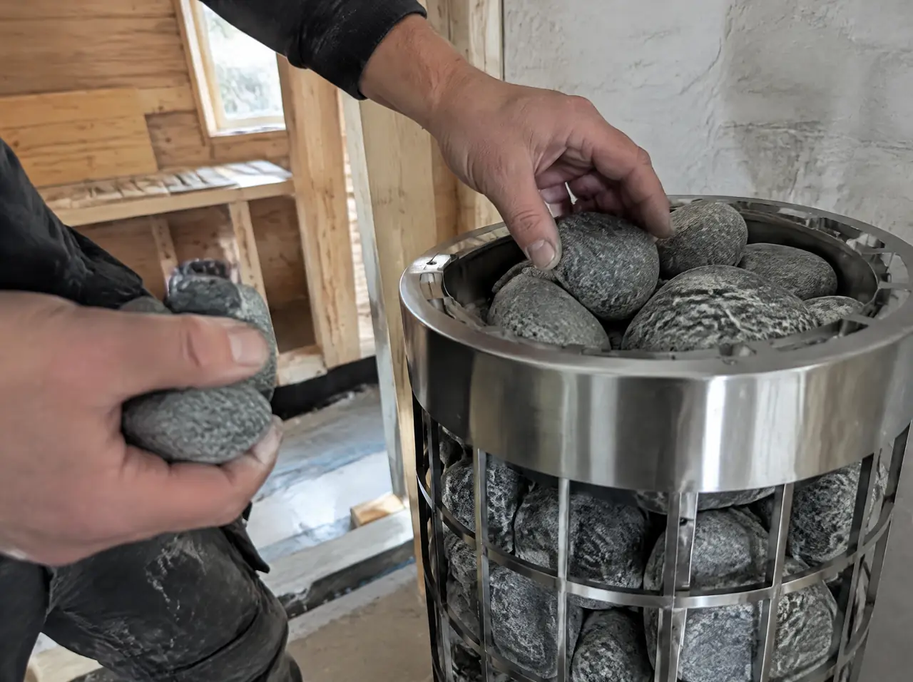 Hands stacking rounded stones into a stainless heater basket