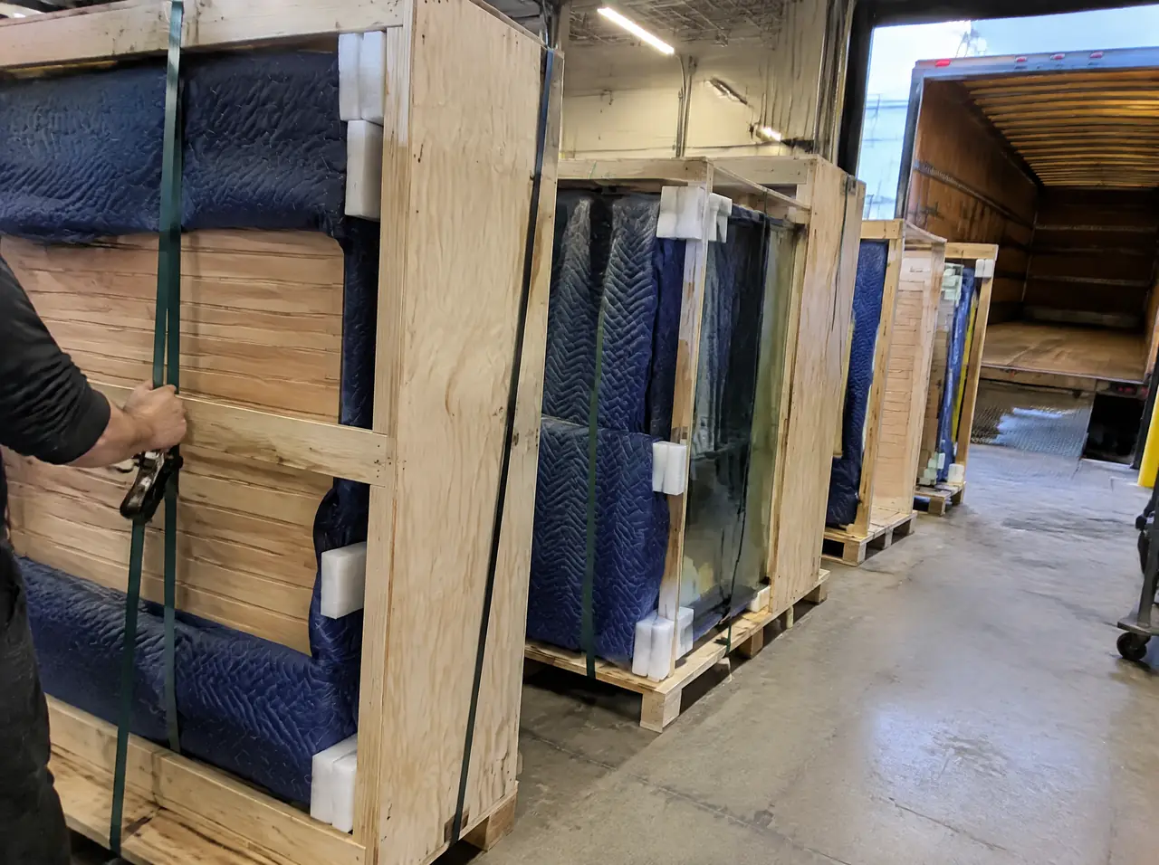 Plywood crates with sauna panels and glass wrapped in blankets at a loading dock